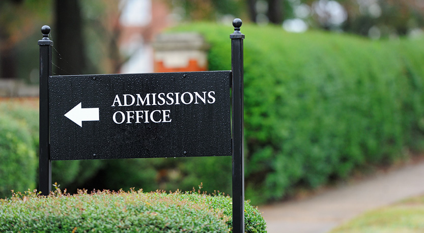 Black sign outside near hedges that reads "admissions office"
