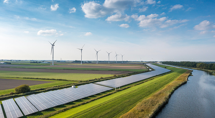 a field of solar panels and wind turbines near a river with a bright blue sky