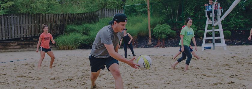 Chris Groeschen serves the ball on a sand volleyball court.