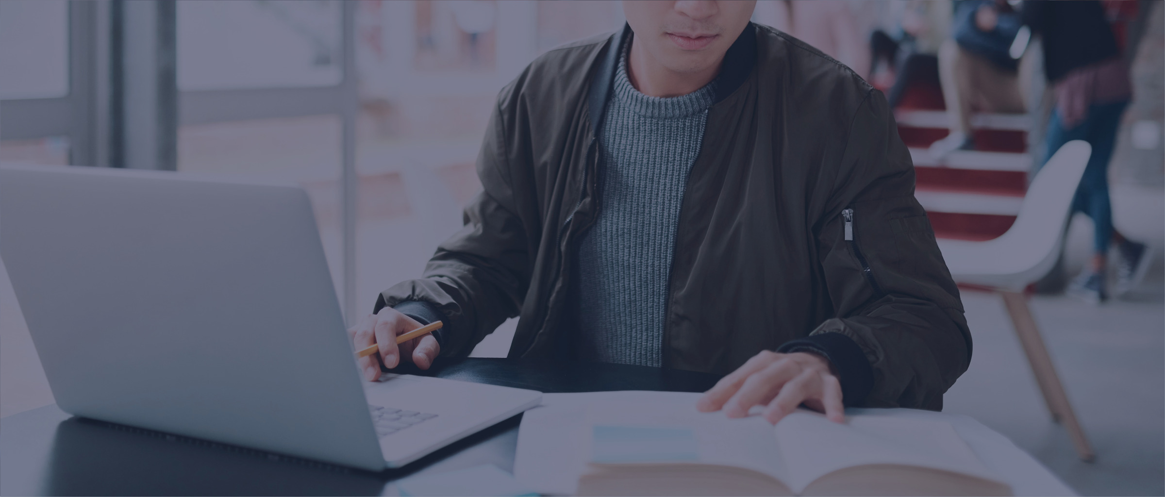 Person sitting at a desk with a book and a laptop our reading.