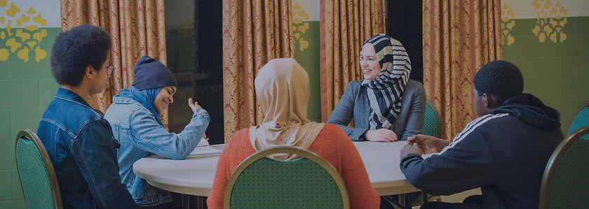 Roula Allouch sits at a table talking with young adults.