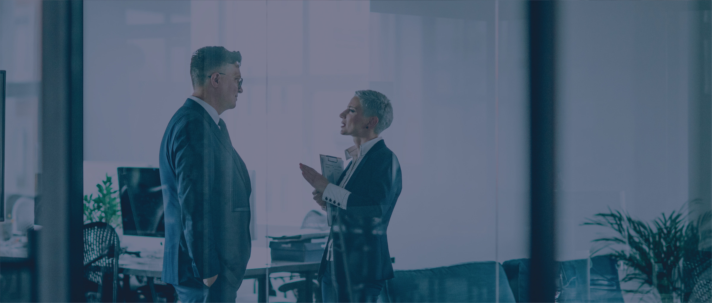 Two people talking behind the glass wall of a conference room