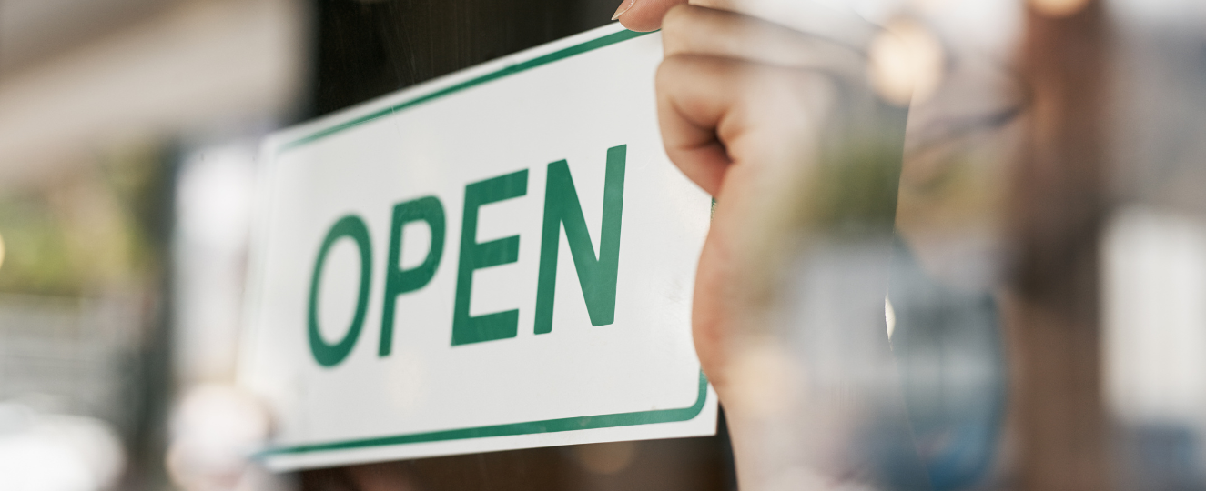 Person hanging an open sign in a window.