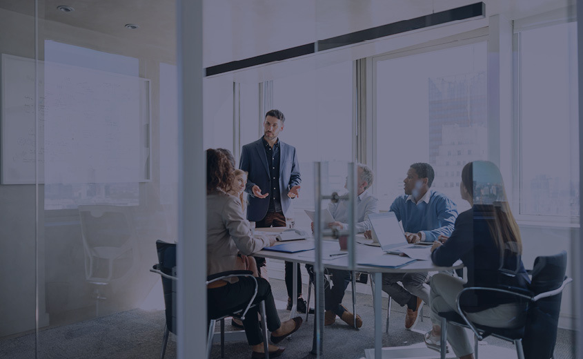 Multiple people sitting at a conference room table and listening to someone talk